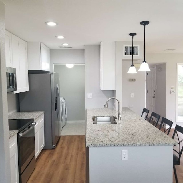 kitchen featuring a kitchen bar, stainless steel appliances, sink, independent washer and dryer, and white cabinetry