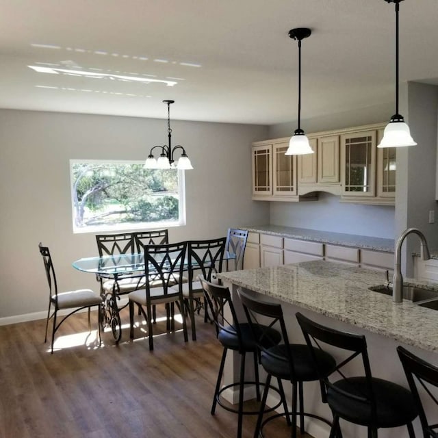 kitchen featuring sink, light stone counters, dark hardwood / wood-style floors, a notable chandelier, and decorative light fixtures