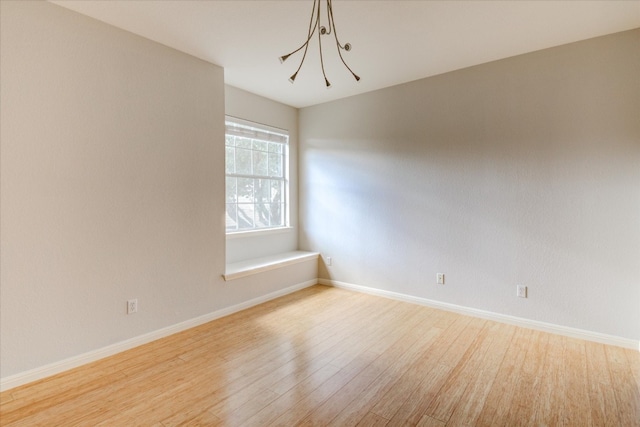 spare room with a chandelier and light wood-type flooring