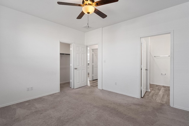 unfurnished bedroom with a spacious closet, a closet, ceiling fan, and light carpet