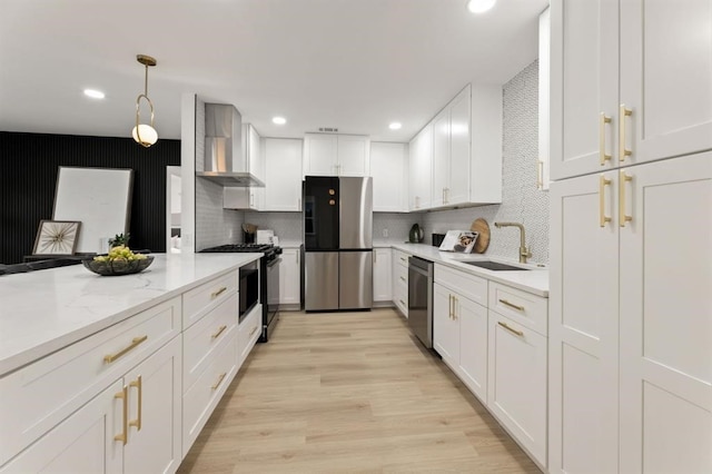 kitchen with white cabinetry, sink, wall chimney range hood, decorative light fixtures, and appliances with stainless steel finishes