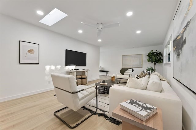 living room featuring ceiling fan, light hardwood / wood-style floors, and a skylight