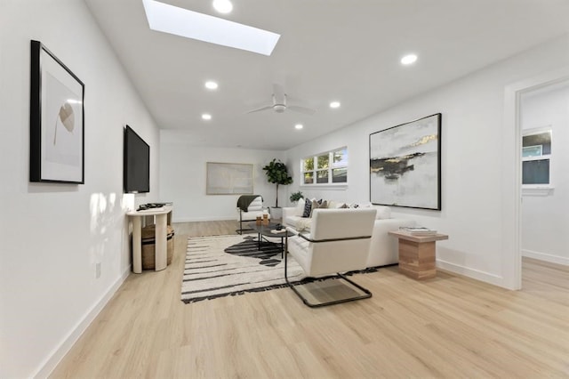 living room featuring a skylight, ceiling fan, and light hardwood / wood-style flooring