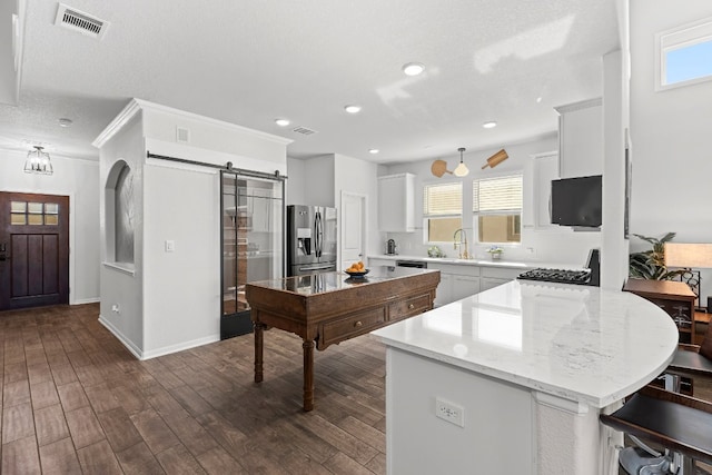 kitchen with a barn door, a healthy amount of sunlight, stainless steel refrigerator with ice dispenser, and dark wood-type flooring