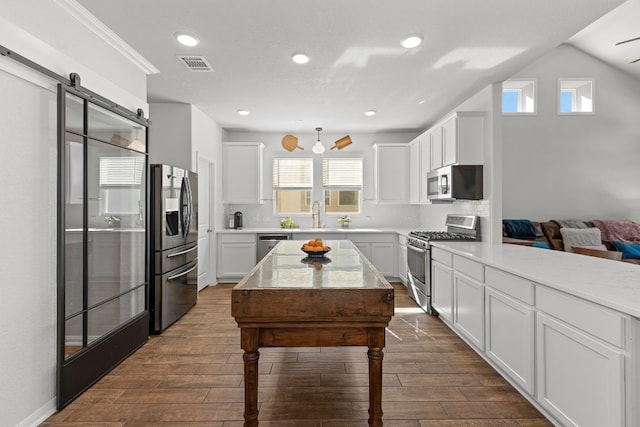 kitchen with a barn door, stainless steel appliances, white cabinetry, and dark wood-type flooring