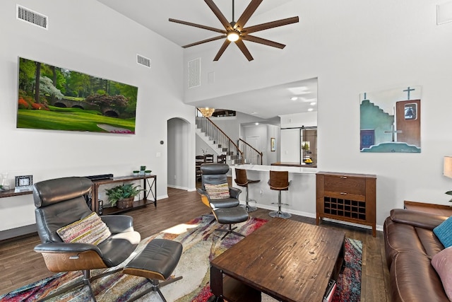 living room with ceiling fan, a barn door, dark hardwood / wood-style flooring, and a towering ceiling