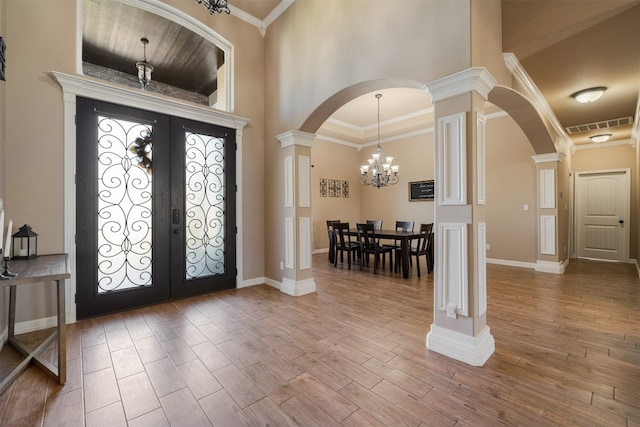 entrance foyer featuring french doors, a towering ceiling, crown molding, an inviting chandelier, and hardwood / wood-style floors