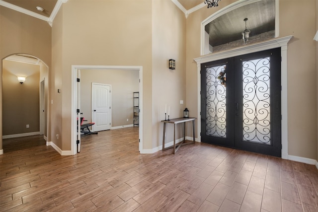 foyer entrance with hardwood / wood-style floors, ornamental molding, a high ceiling, and french doors