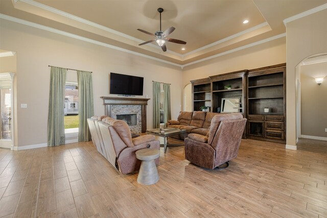 living room featuring a tray ceiling, crown molding, a fireplace, and light hardwood / wood-style flooring