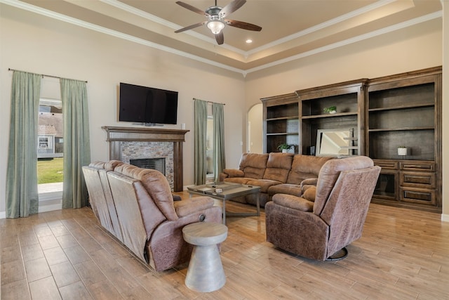 living room with a fireplace, light wood-type flooring, a tray ceiling, and ornamental molding