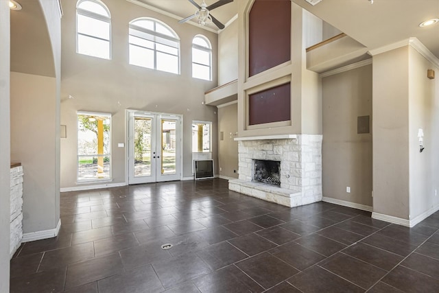 unfurnished living room featuring a stone fireplace, dark tile patterned floors, ornamental molding, ceiling fan, and french doors