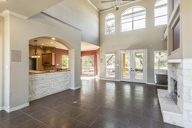 unfurnished living room featuring crown molding, a stone fireplace, french doors, and a towering ceiling