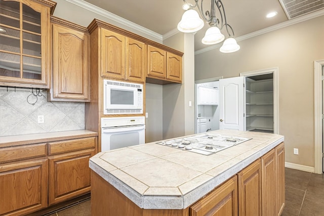 kitchen with white appliances, hanging light fixtures, a center island, ornamental molding, and tile countertops