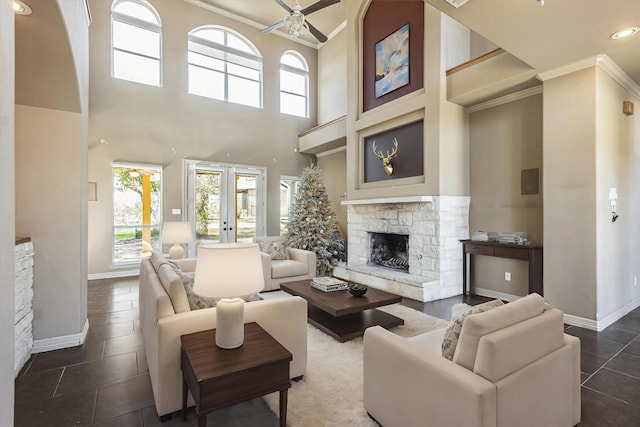 tiled living room with crown molding, ceiling fan, a high ceiling, a stone fireplace, and french doors