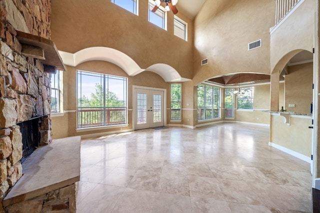 unfurnished living room with ceiling fan, a fireplace, a towering ceiling, and french doors