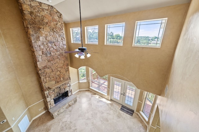 unfurnished living room with french doors, high vaulted ceiling, a stone fireplace, and ceiling fan