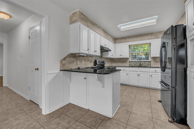 kitchen with black refrigerator, white cabinets, kitchen peninsula, and stainless steel stove