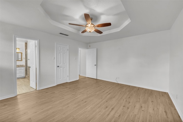 unfurnished bedroom with ensuite bathroom, light hardwood / wood-style floors, a raised ceiling, and ceiling fan