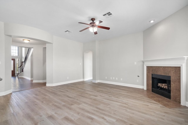 unfurnished living room featuring a tile fireplace, light hardwood / wood-style floors, and ceiling fan