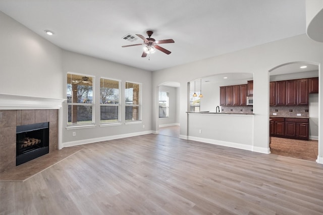 unfurnished living room with a tile fireplace, ceiling fan, sink, and light hardwood / wood-style floors