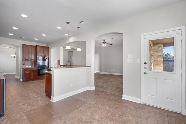 kitchen featuring ceiling fan, sink, double oven, backsplash, and decorative light fixtures