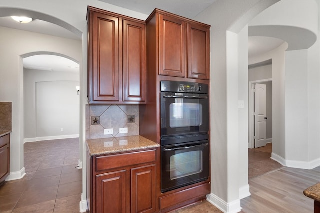 kitchen with light stone countertops, light wood-type flooring, backsplash, and black double oven