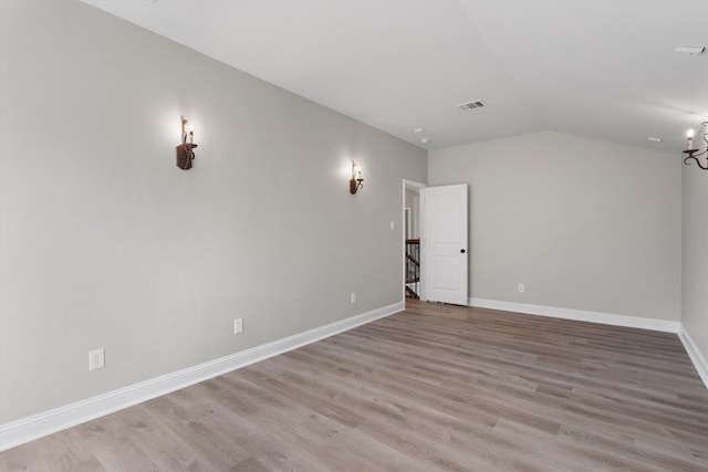 unfurnished room with light hardwood / wood-style flooring, a chandelier, and vaulted ceiling