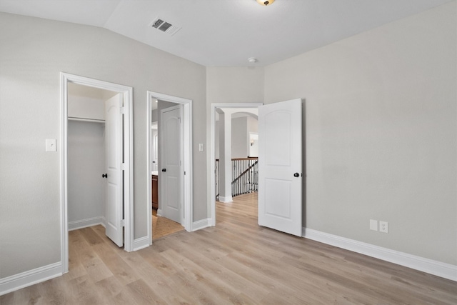 unfurnished bedroom featuring lofted ceiling, light wood-type flooring, a walk in closet, and a closet