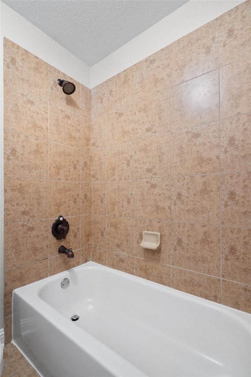 bathroom featuring a textured ceiling and tiled shower / bath