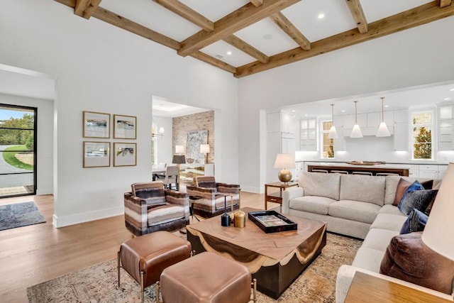 living room featuring beamed ceiling, a high ceiling, an inviting chandelier, and light wood-type flooring