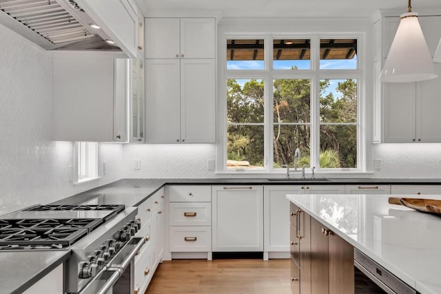 kitchen featuring high end stainless steel range, sink, hanging light fixtures, custom range hood, and white cabinets