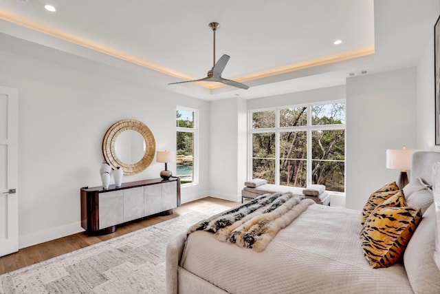 bedroom featuring a raised ceiling, ceiling fan, and light wood-type flooring