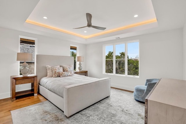 bedroom featuring a tray ceiling, ceiling fan, and light wood-type flooring