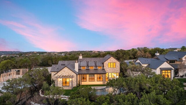 4312 Amarra Dr, Austin, TX 78735 - back of house at dusk with a standing seam roof, a patio, stone siding, metal roof, and a chimney