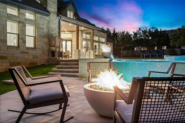 pool at dusk with pool water feature, a patio, a fire pit, and a trampoline