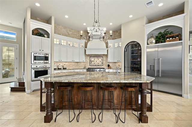 kitchen with built in appliances, a spacious island, a breakfast bar area, decorative backsplash, and white cabinets