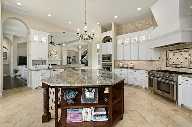 kitchen with premium range hood, a large island with sink, ceiling fan with notable chandelier, hanging light fixtures, and appliances with stainless steel finishes