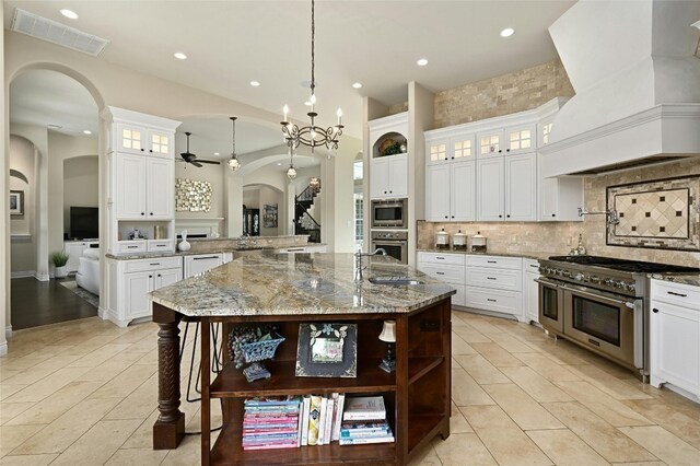 12920 Zen Gardens Way, Austin, TX 78732 - kitchen featuring open shelves, appliances with stainless steel finishes, custom range hood, arched walkways, and recessed lighting