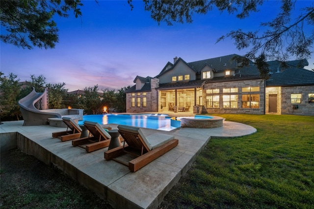 pool at dusk featuring a lawn, an in ground hot tub, and a water slide