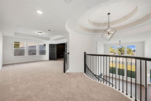 hallway featuring visible vents, a tray ceiling, carpet flooring, an upstairs landing, and a chandelier