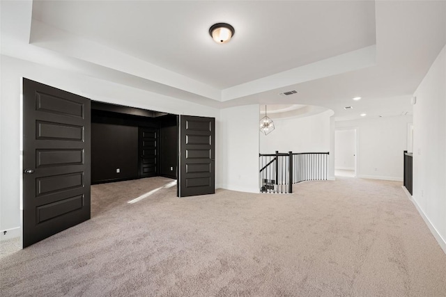 carpeted empty room with a tray ceiling, visible vents, baseboards, and recessed lighting