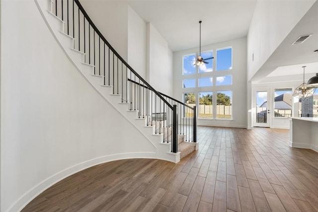 entryway featuring a towering ceiling, stairway, wood finished floors, baseboards, and ceiling fan with notable chandelier