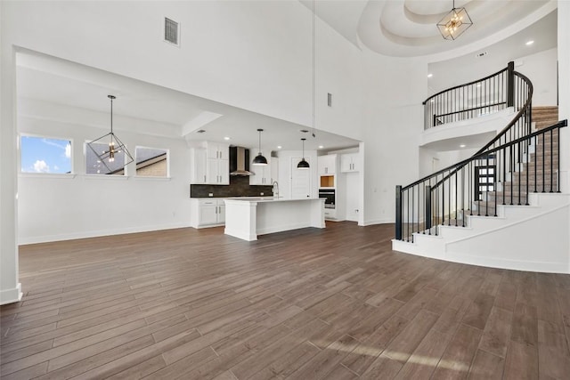 unfurnished living room with a chandelier, a tray ceiling, stairway, and dark wood finished floors