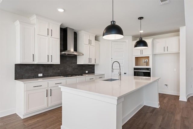 kitchen featuring tasteful backsplash, white cabinets, a sink, black appliances, and wall chimney exhaust hood