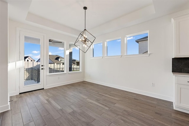 unfurnished dining area with a notable chandelier, baseboards, a raised ceiling, and dark wood-style flooring