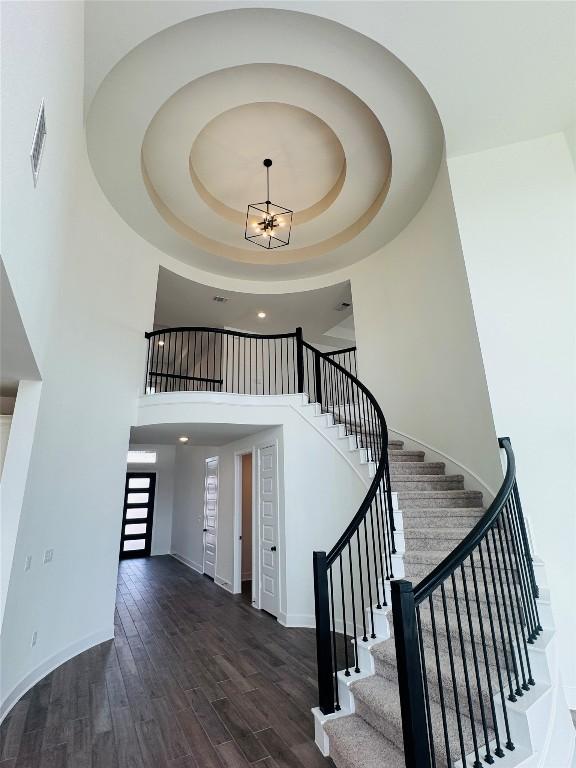 1205 Summer Moon Dr, Georgetown, TX 78628 - stairway featuring wood finished floors, baseboards, a raised ceiling, a high ceiling, and a chandelier