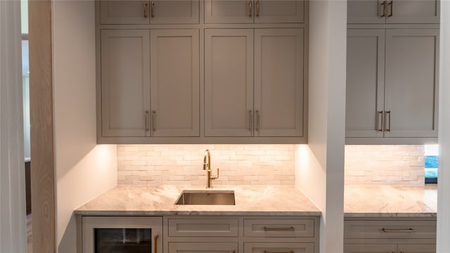 bar featuring backsplash, gray cabinets, light stone counters, and sink