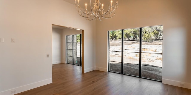 unfurnished room with an inviting chandelier, baseboards, and wood finished floors