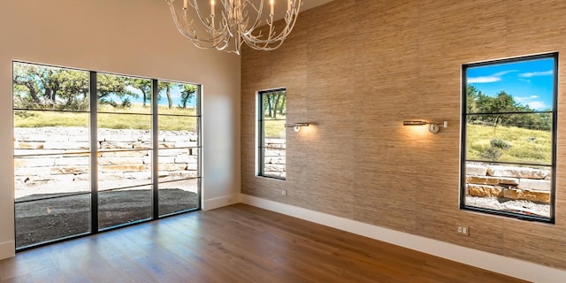 spare room featuring baseboards, wood finished floors, a towering ceiling, and an inviting chandelier