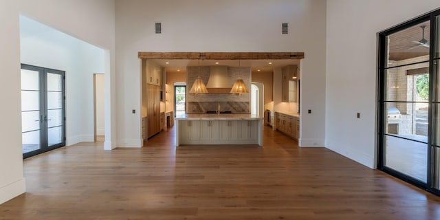 kitchen featuring french doors, light countertops, a towering ceiling, wood finished floors, and wall chimney exhaust hood